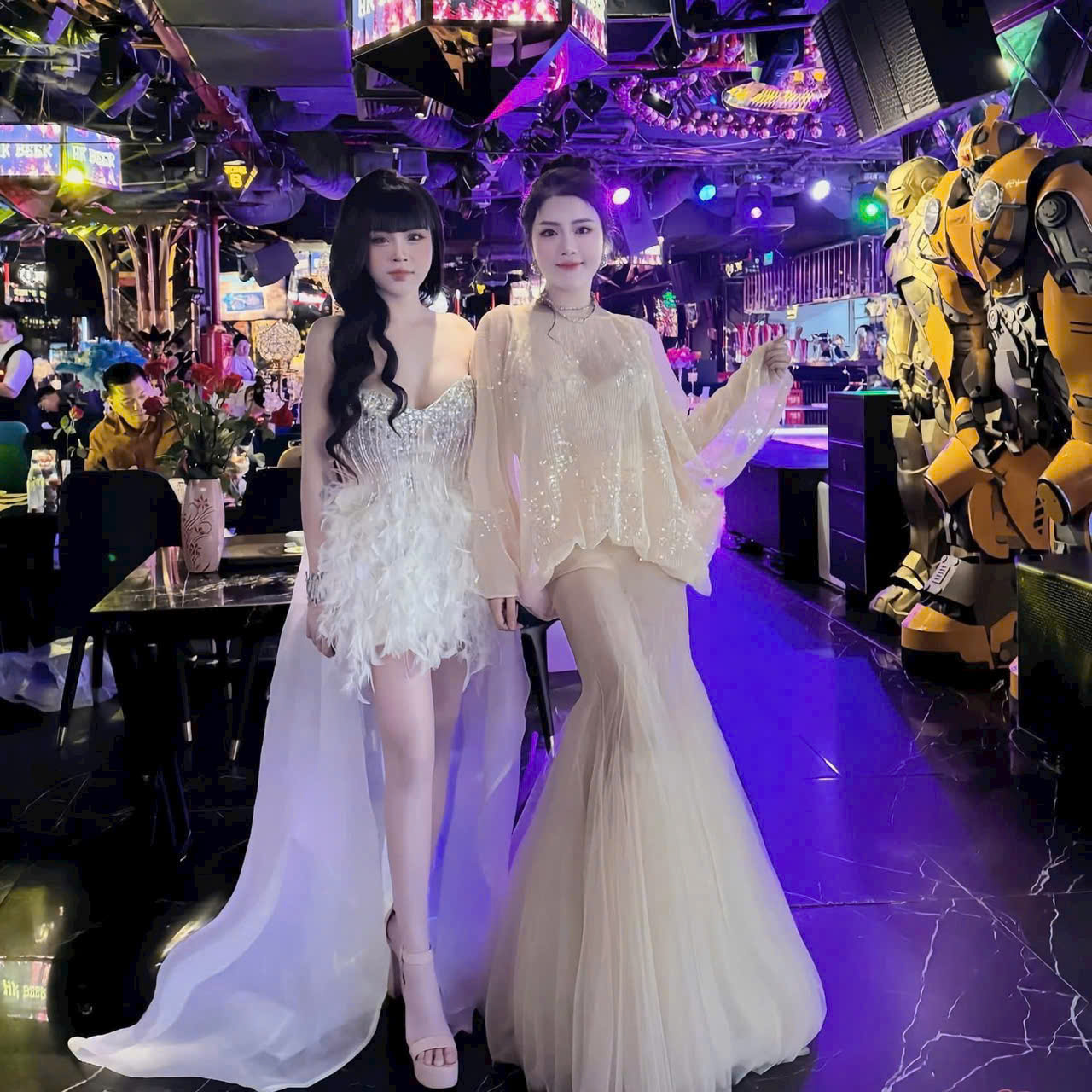 Hai nhân viên trong trang phục lông vũ hồng tại lối vào dát vàng của quán